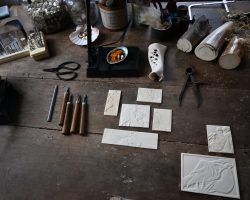 Werkstattambiente, ein Arbeitsplatz mit mehreren kleinen Reliefs und Schnitzwerkzeug