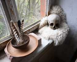 Werkstattambiente, eine Fensterbank, ein altes Fenster, eine Räucherschale mit Raubvogelfedern und ein menschlicher Schädel